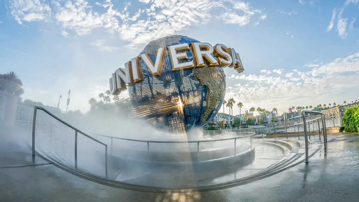 Universal Studios globe surrounded by mist and palm trees under a blue sky with scattered clouds.