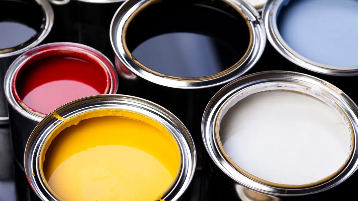 Open paint cans filled with vibrant red, yellow, white, black, and blue colors ready for use.