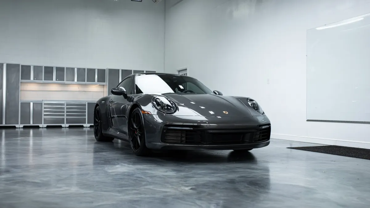 Gray Porsche sports car parked indoors in a modern garage with polished concrete floor and industrial lighting.