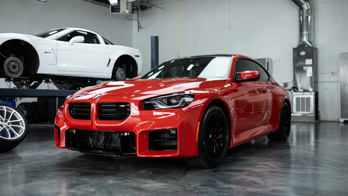 Red sports car parked in a modern garage with a white car on a lift in the background.