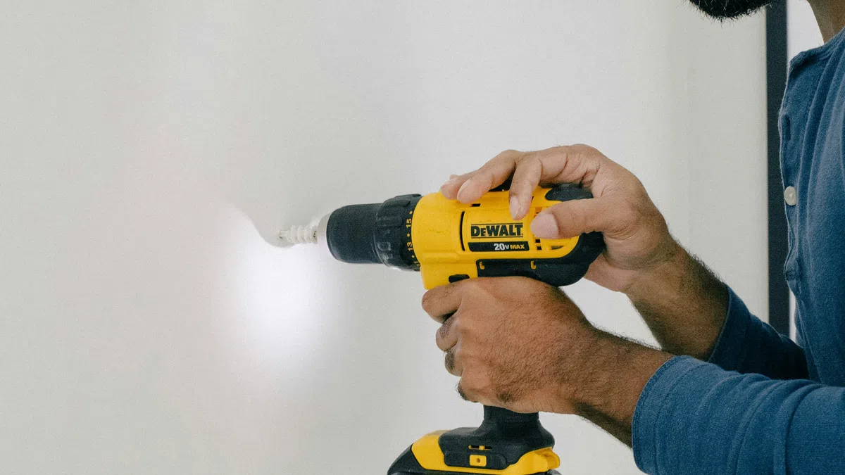 Man using a yellow DeWalt cordless drill to drill into a white wall with built-in LED light.