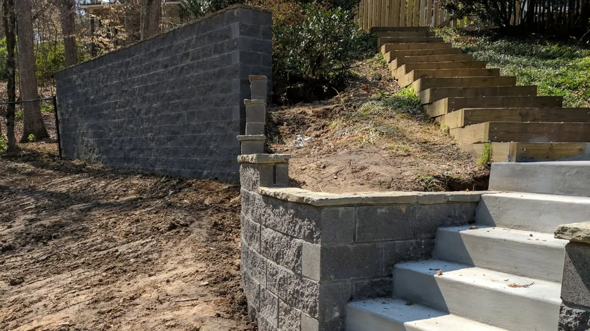 Outdoor concrete stairs leading up a slope with retaining walls and wooden steps in a wooded residential backyard.