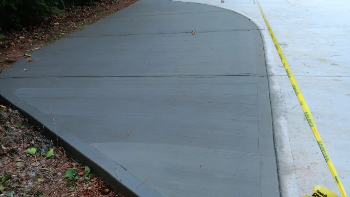 Freshly poured concrete driveway with wet and dry sections cordoned off by caution tape and wooden stakes.