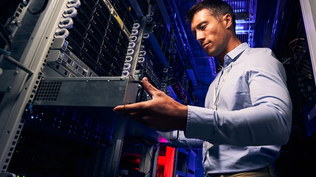 IT technician installing or removing a server unit in a data center rack with blue and red lighting.