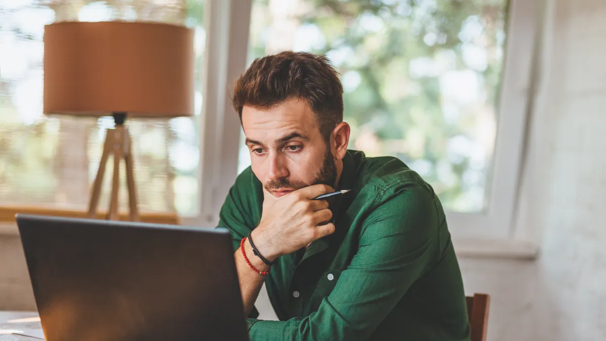 a person sitting at a table with a laptop and smoking a cigarette