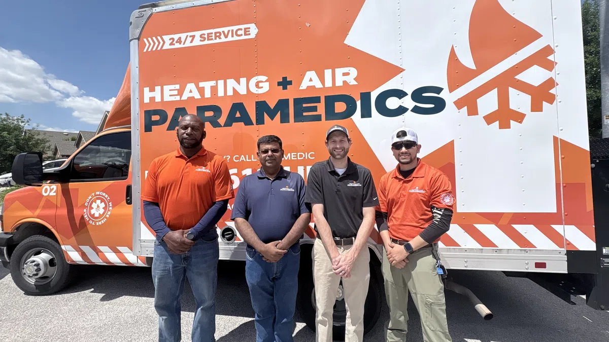Four heating and air paramedics standing in front of their branded service truck with clear sky background