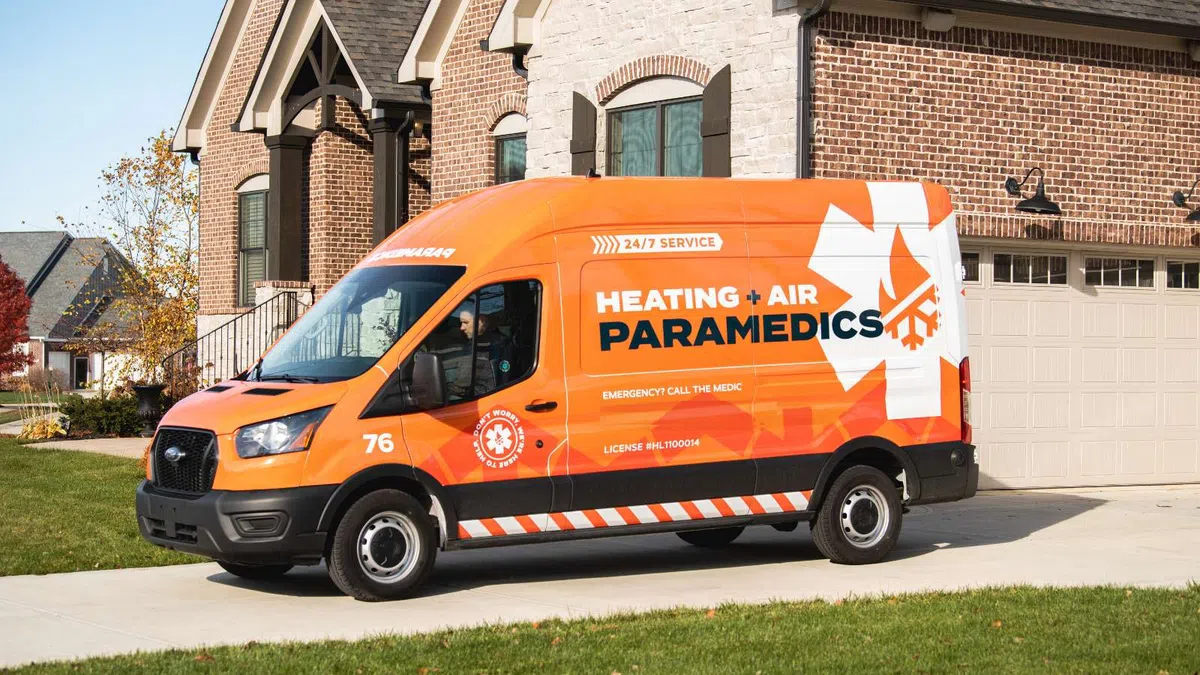 Orange Heating + Air Paramedics service van parked in driveway of suburban brick house on clear day