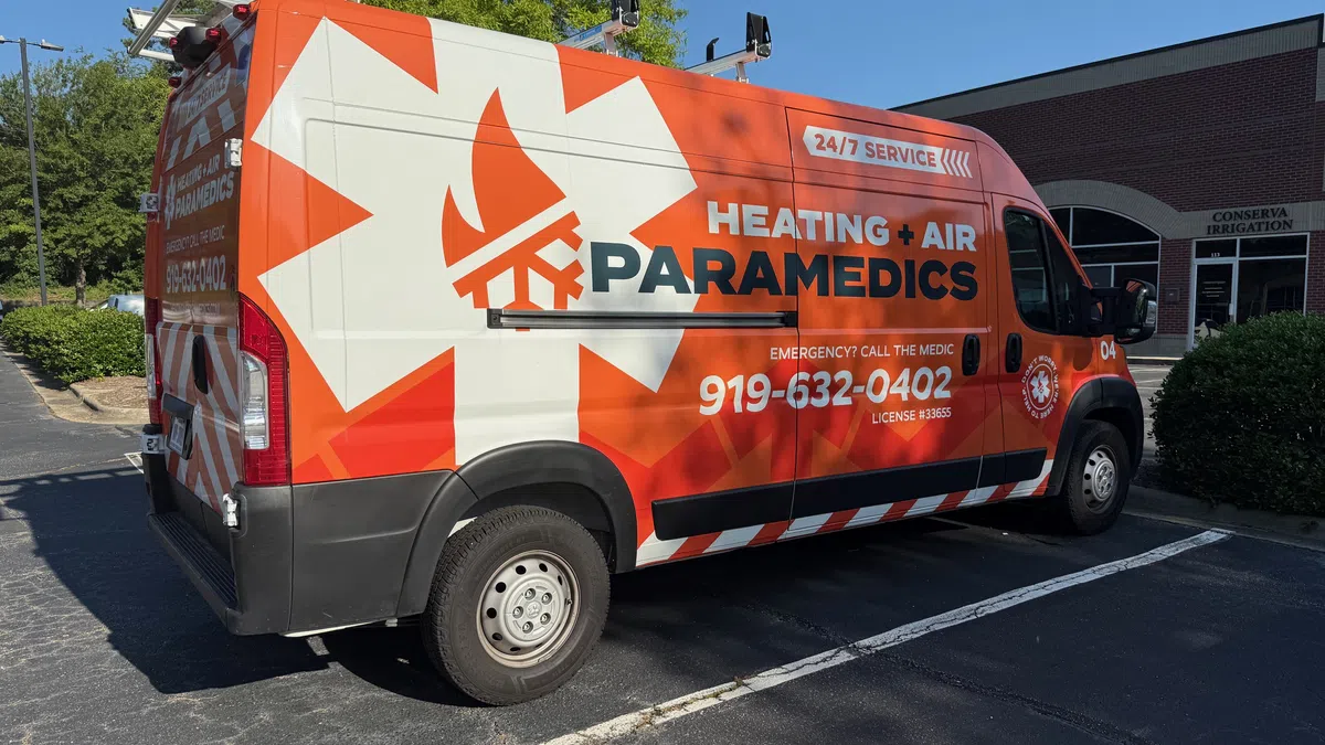 Orange and white Heating Air Paramedics service van parked, displaying emergency phone number and 24/7 service text.