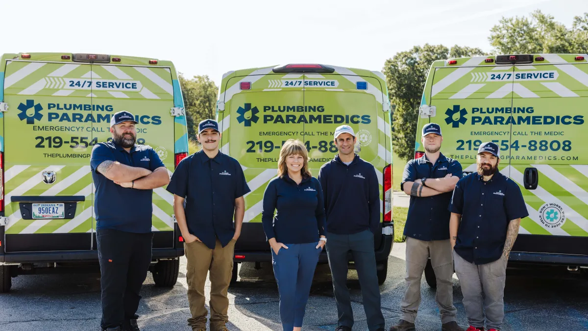 Plumbing Paramedics team standing in front of branded service vans with contact information visible on sunny day.