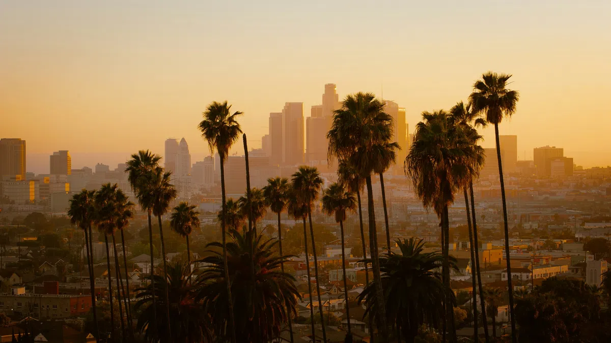 Sunset over a city skyline with palm trees silhouetted against a golden sky in the foreground.