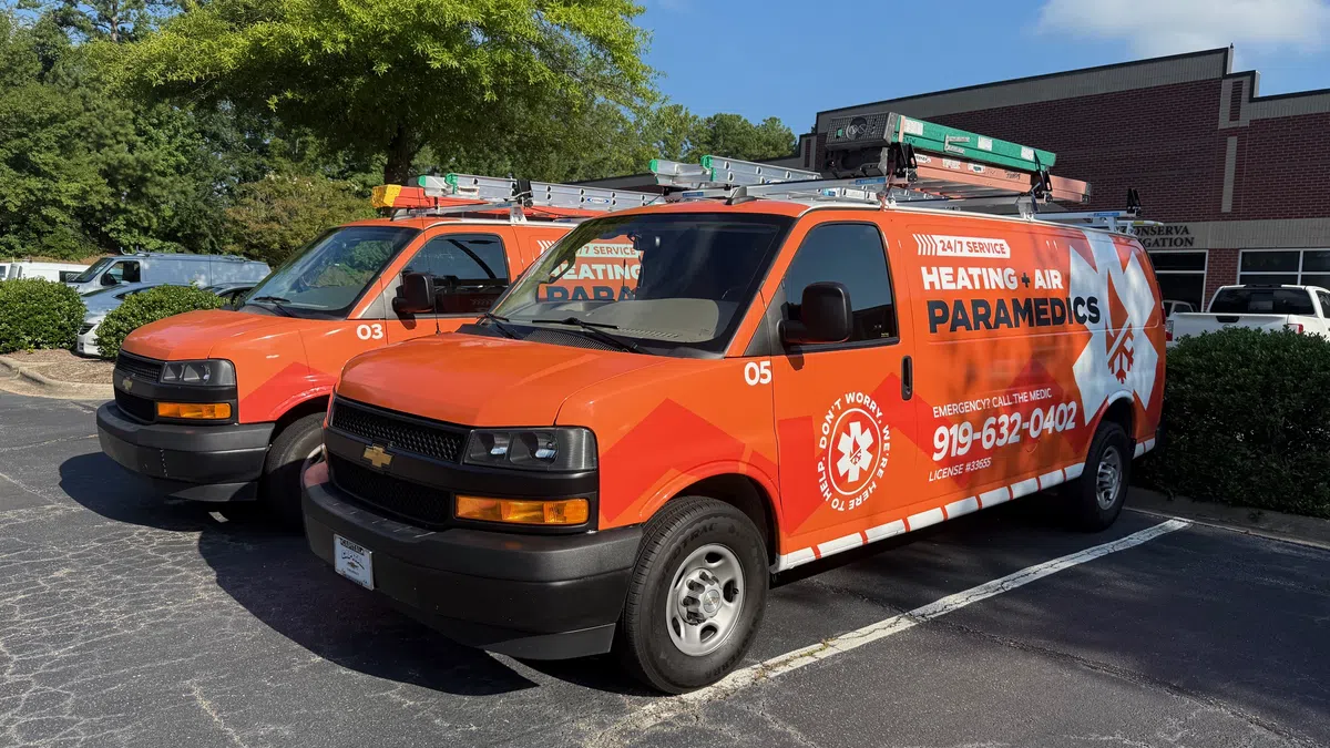 Two bright orange Heating and Air Paramedics service vans parked in a lot on a sunny day.