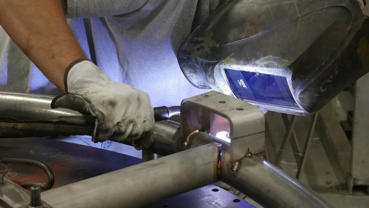 A welder in protective gear works on metal pipes with sparks flying in a workshop setting.