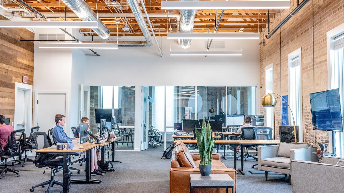 Modern open office with exposed wooden beams, desks, seating area, and people working at computers