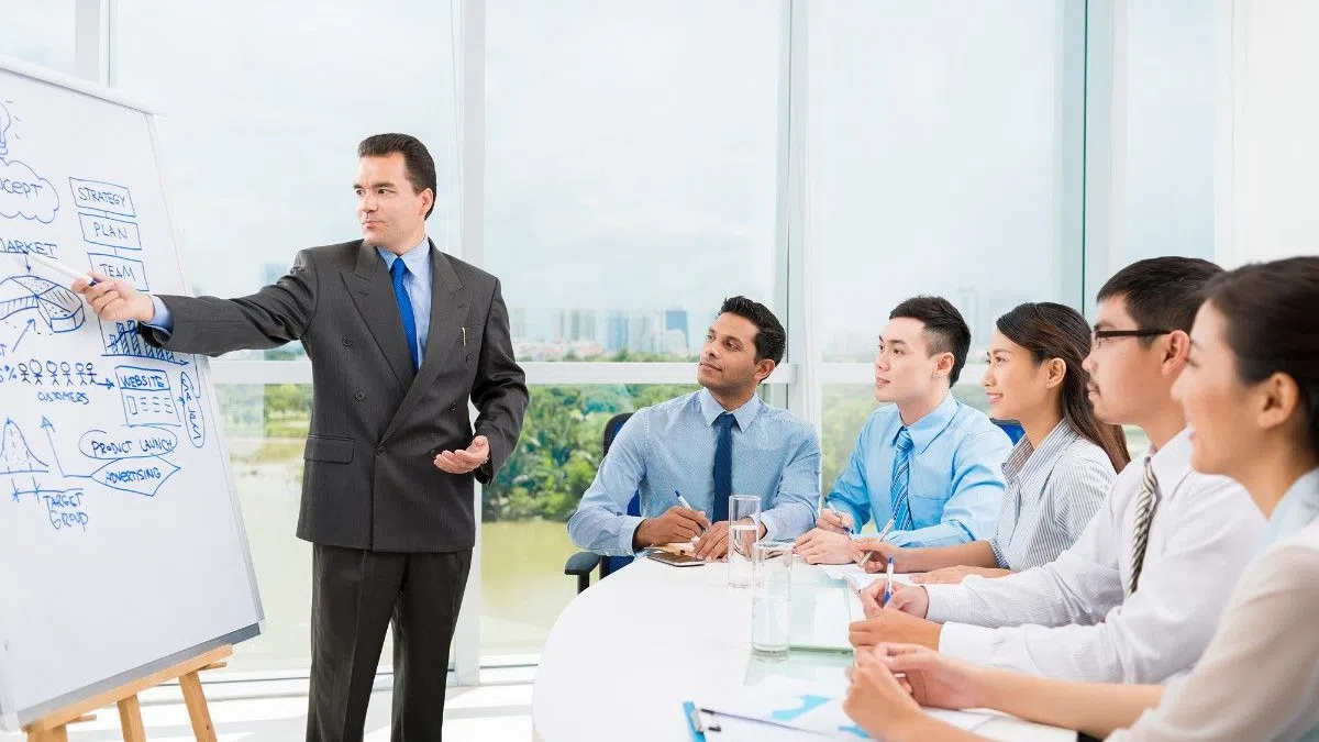Businessman presenting strategy and marketing plan on whiteboard to attentive team in modern office