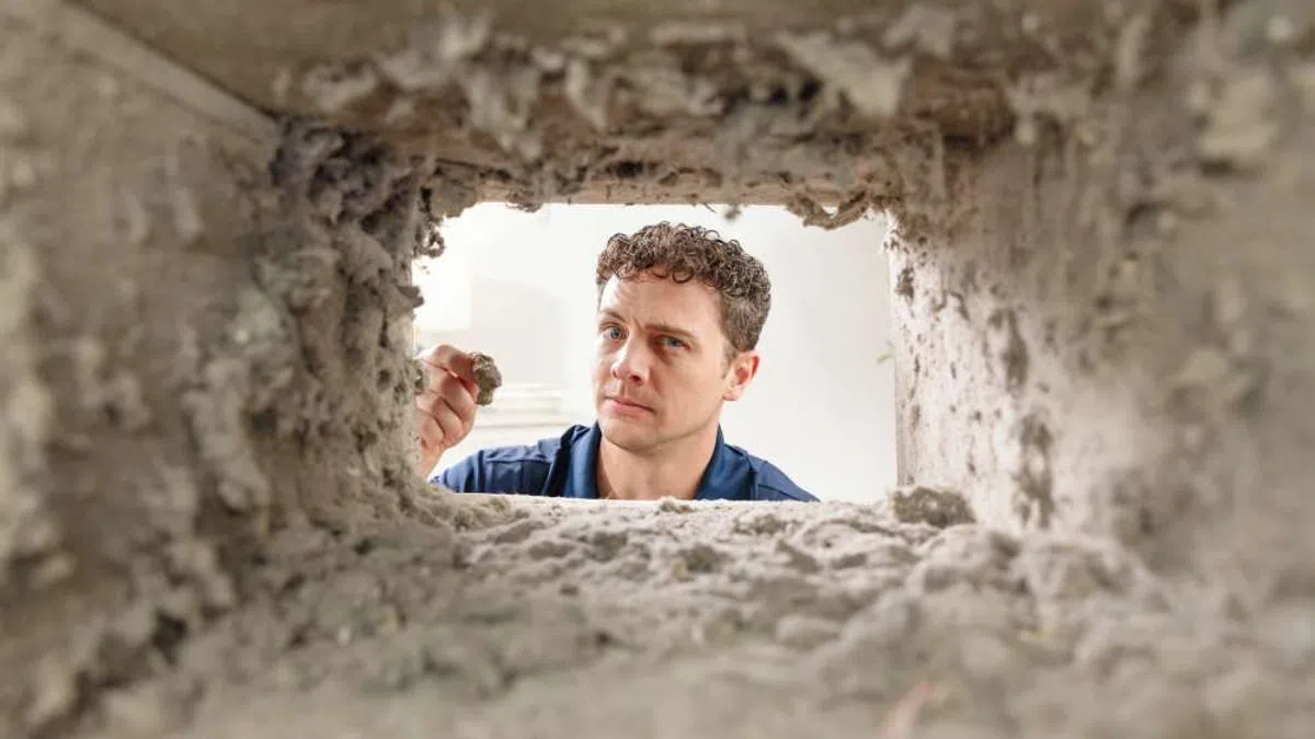 Man inspecting concrete core sample through rectangular hole in concrete wall under bright light