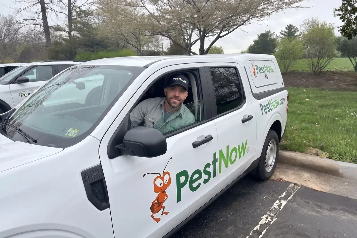 PestNow technician sitting in a white company truck with PestNow logo parked in a lot next to a grassy area.