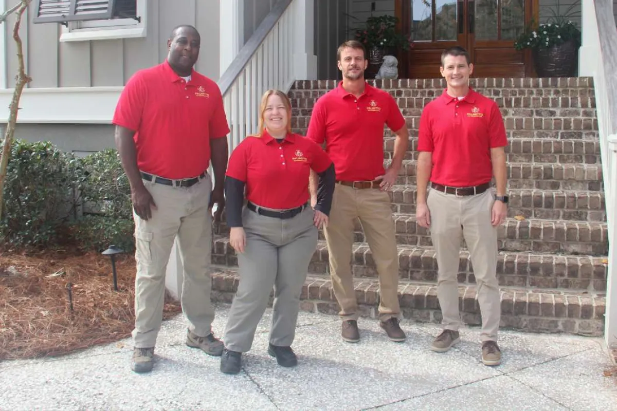Four people in red polo shirts and khaki pants posing in front of a brick staircase and house entrance