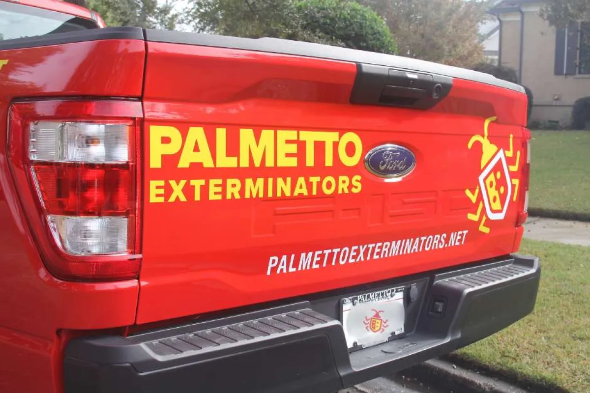 Red Ford pickup truck with Palmetto Exterminators logo and contact website on the tailgate in yellow and white lettering.