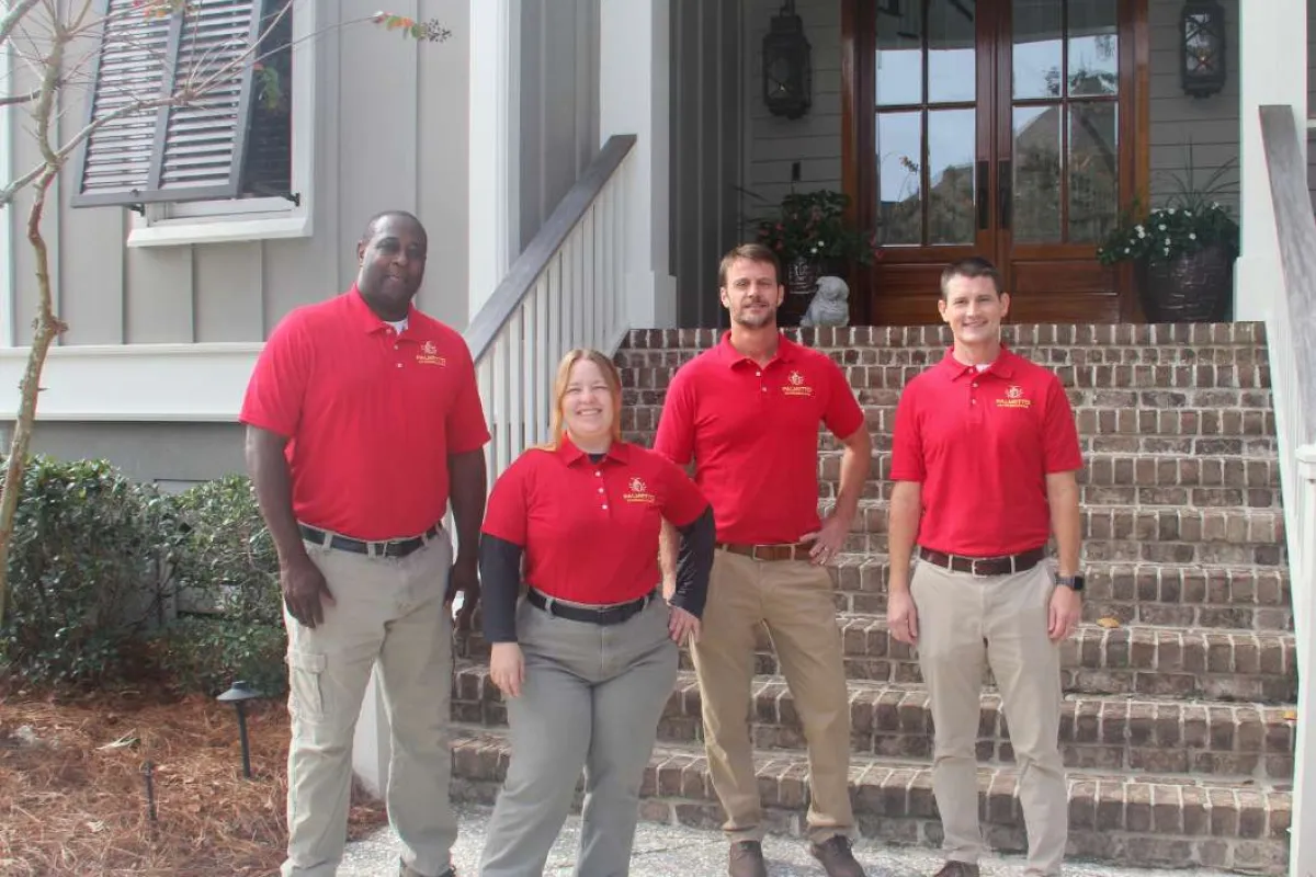 Four professionals wearing red shirts and khaki pants standing outside a residential home with brick steps.