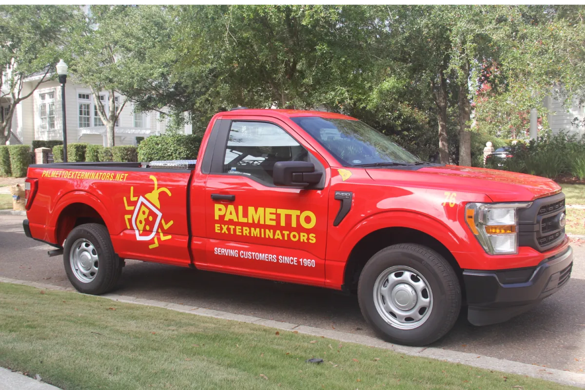 Red Palmetto Exterminators truck parked on a suburban street with company logo and contact details visible.