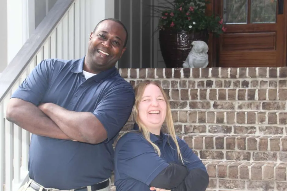 Two smiling security guards in uniform posing confidently with crossed arms on a brick staircase outside a building.