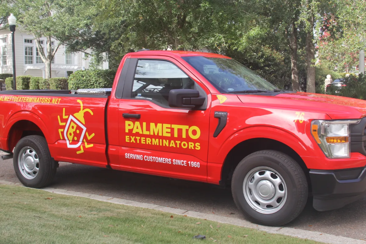 Red Palmetto Exterminators truck parked outside with company logo and contact information visible
