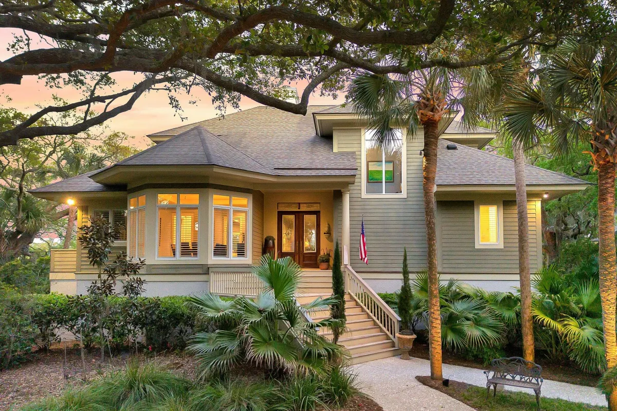 Modern gray house with large windows and stairs surrounded by lush palm trees at sunset.