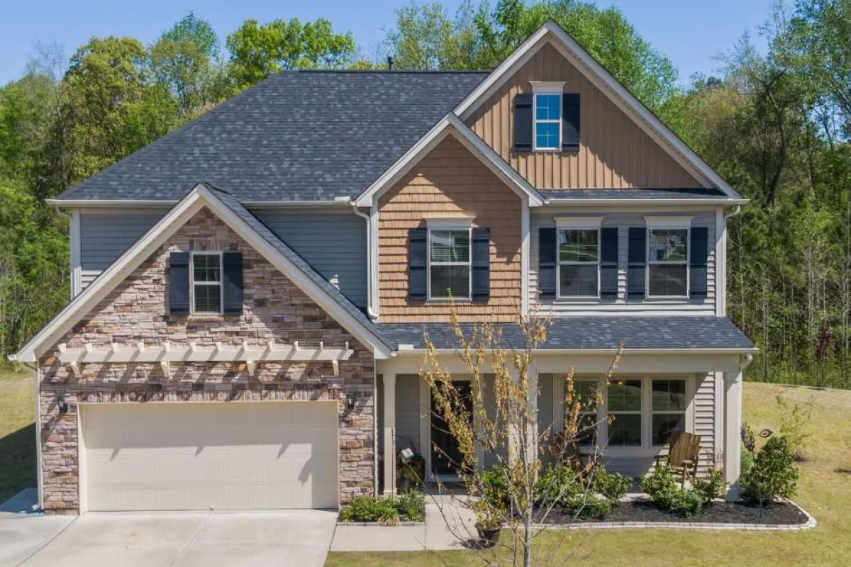 Two-story suburban house with mixed stone and siding exterior, front porch, garage, and landscaped yard.