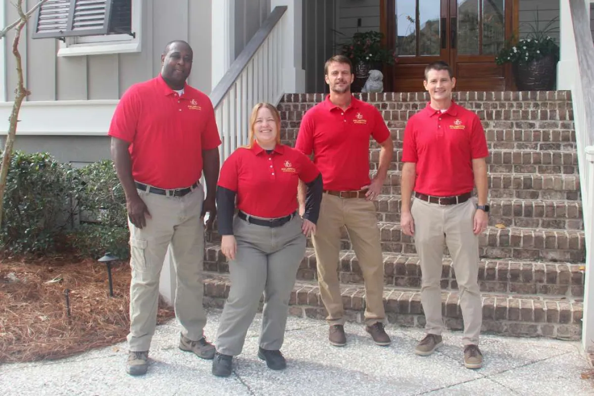 Four professionals in red polo shirts and khaki pants posing outside a house with brick steps and a wooden door.