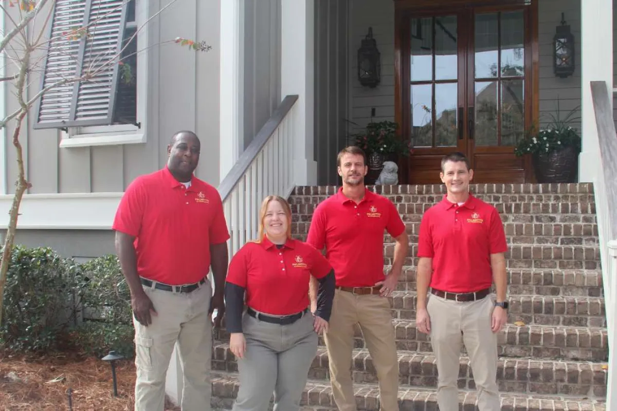 Four professional team members in red polo shirts standing outside a house entrance with brick steps.