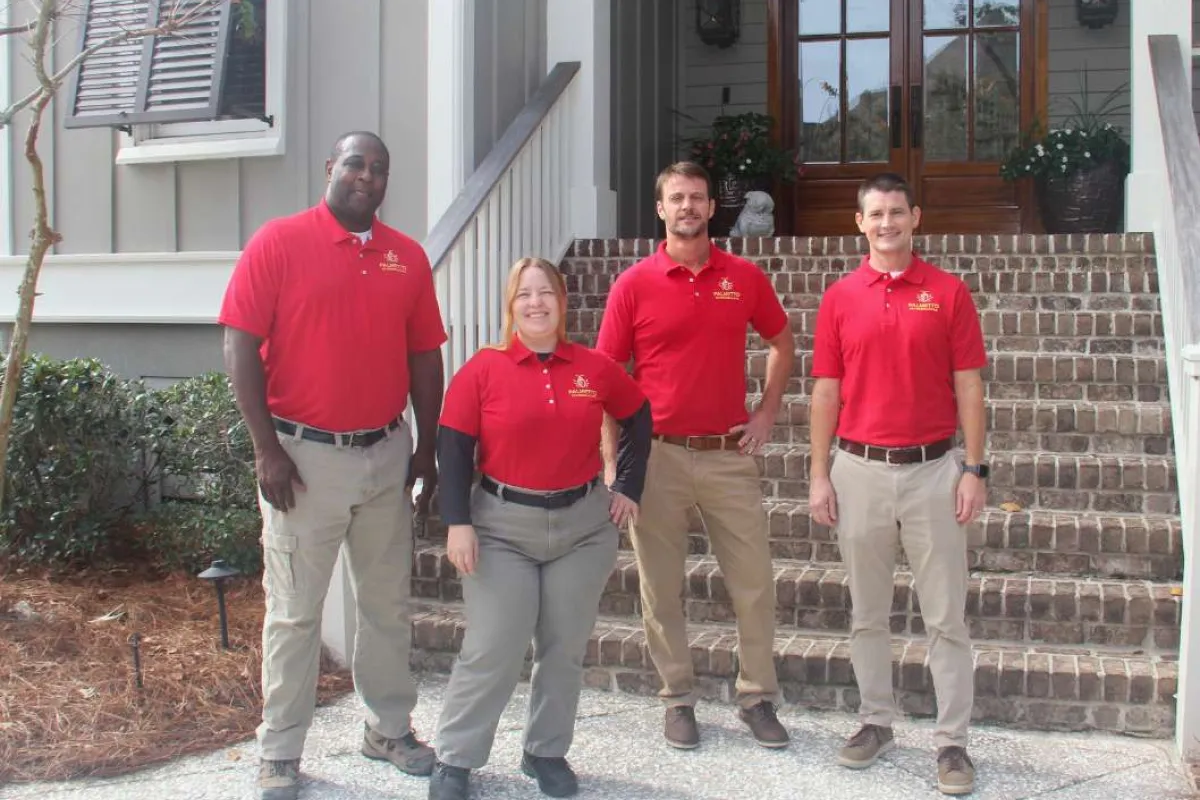 Four professionals in red polo shirts standing confidently outside a residential home with brick stairs and wooden doors.