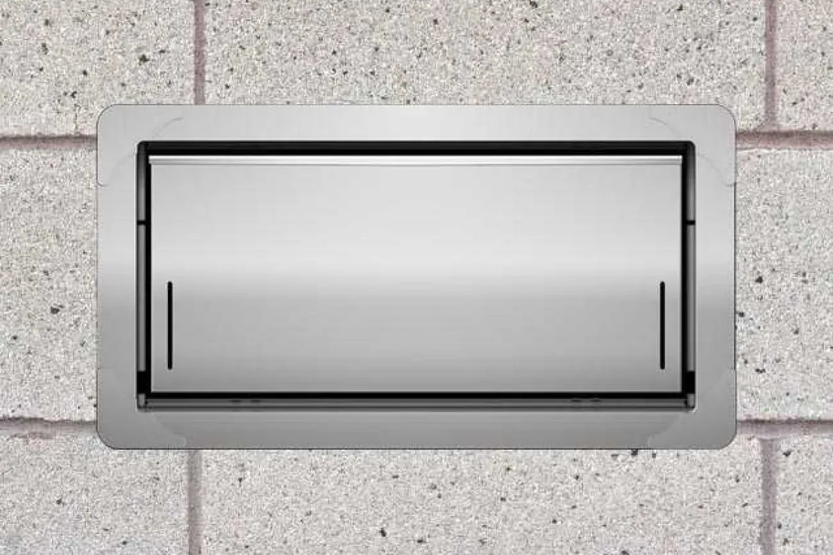 Rectangular stainless steel wall vent installed on a light gray concrete block wall outdoors.