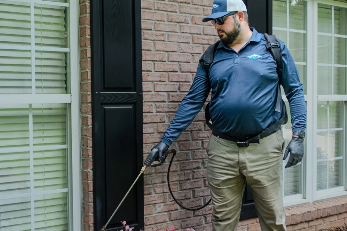 Ozane Pest control technician in uniform spraying near house foundation in Monmouth County