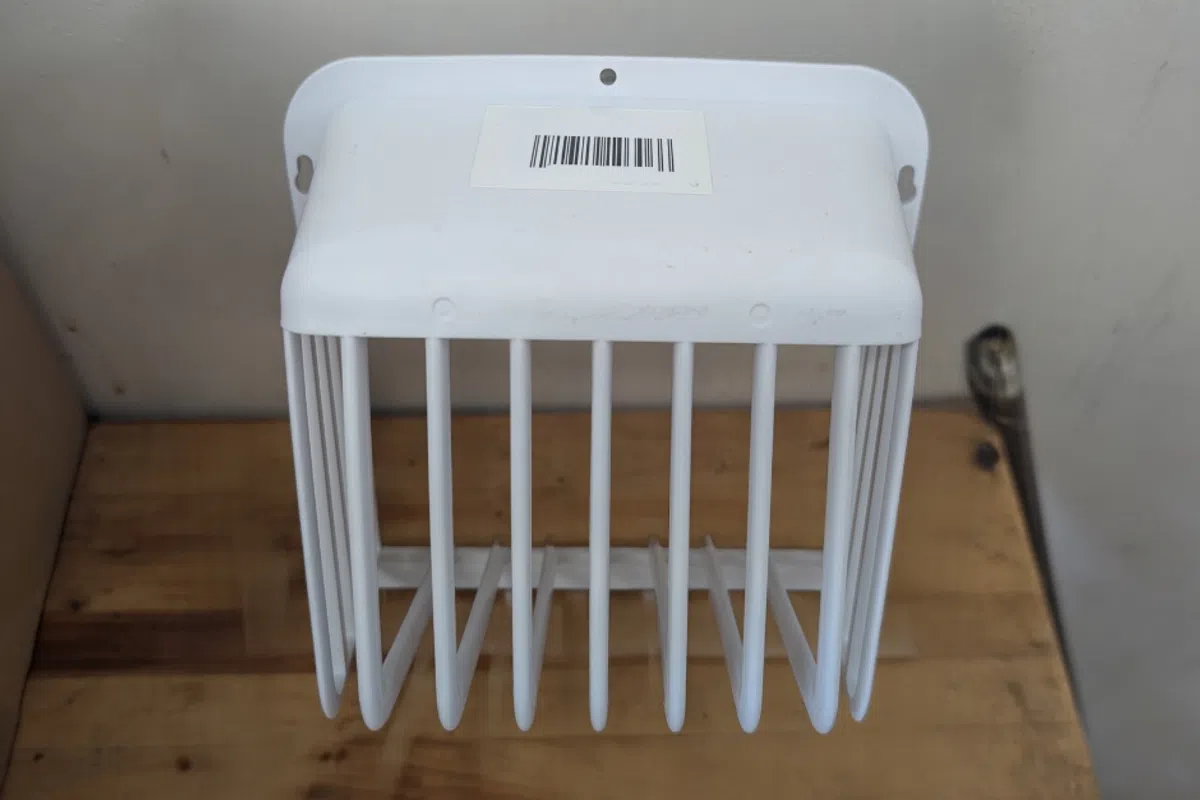 White plastic wall-mounted holder with vertical slots on wooden surface against white wall.