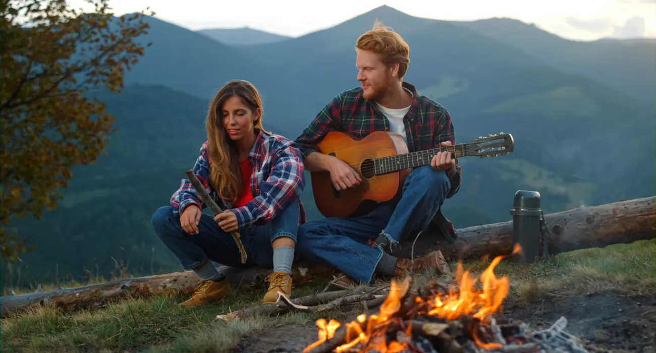 Couple enjoying music by a campfire in the mountains during sunset.
