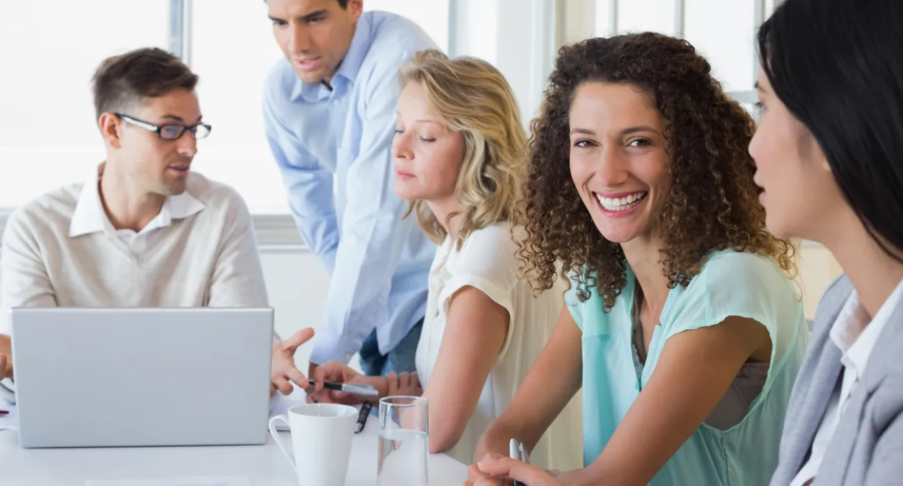 Group of five professionals engaged in a collaborative meeting around a table with laptop and documents.