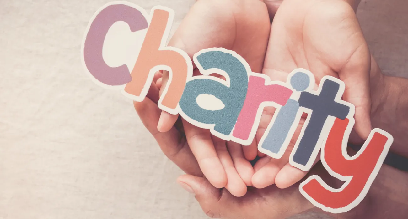 Adult and child hands holding colorful letters spelling charity, symbolizing support and giving.