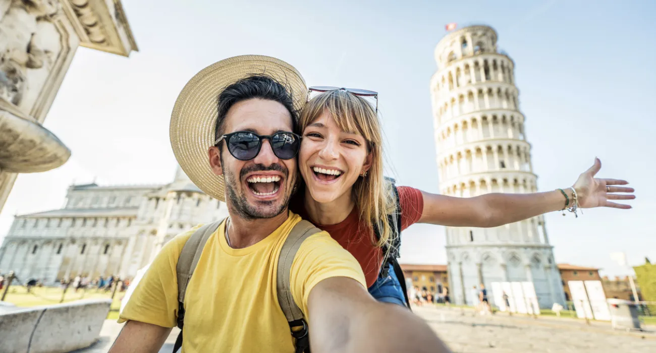 Happy young couple taking a selfie with the Leaning Tower of Pisa in Italy on a sunny day