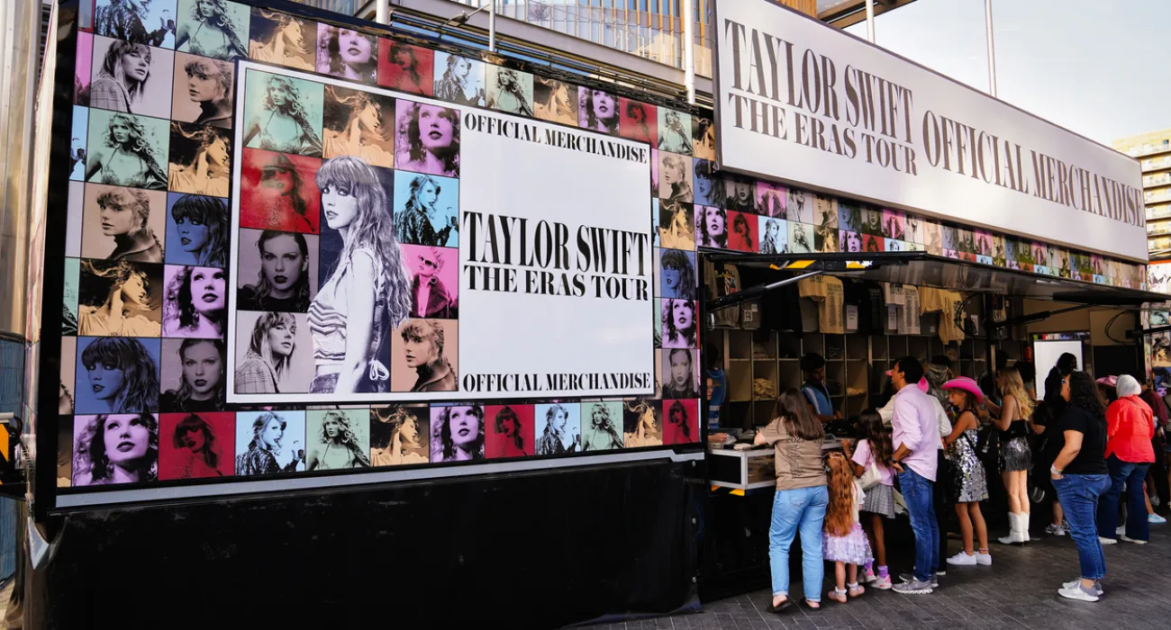 Taylor Swift The Eras Tour official merchandise stand with fans queuing to buy items outdoors.
