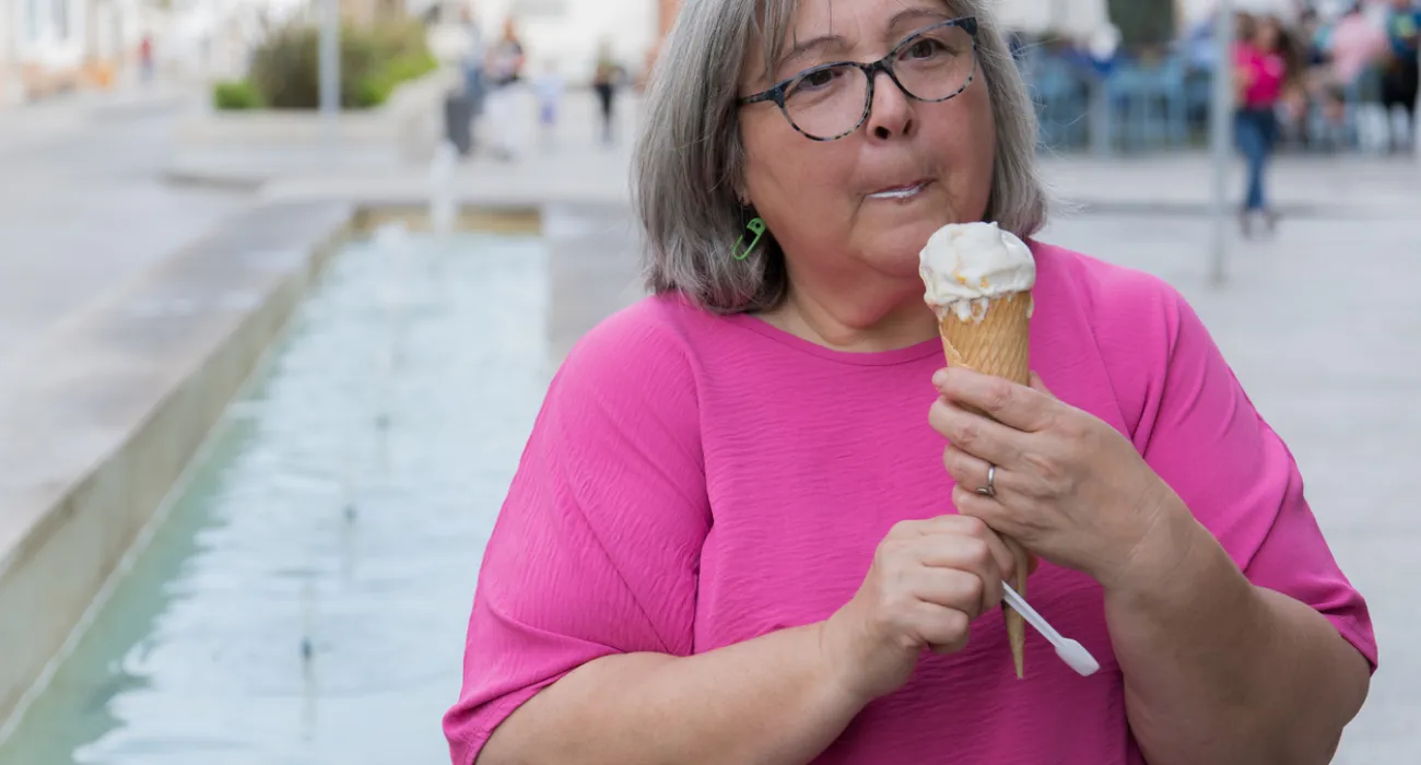 Woman in pink shirt enjoying a vanilla ice cream cone outdoors near a water feature on a sunny day