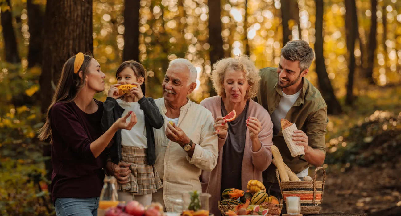 Multigenerational family enjoying autumn picnic in forest with fresh fruit and bread on wooden table.