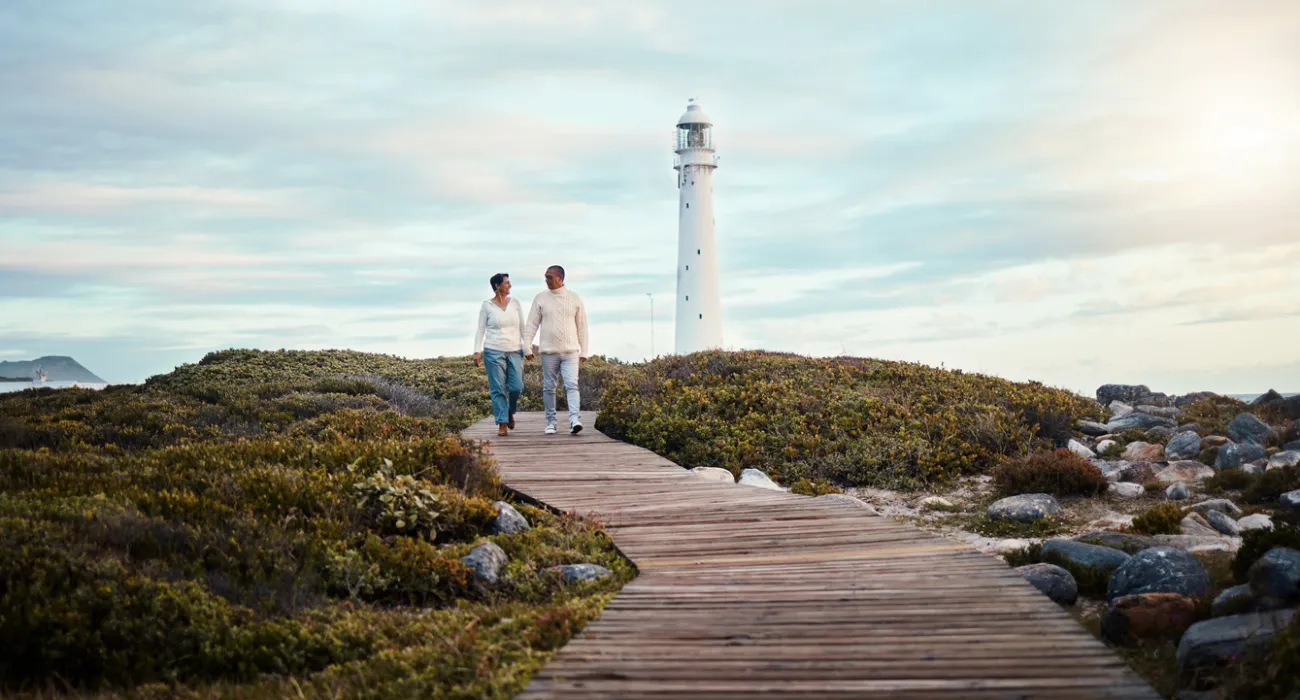 a man and woman walking on a wooden path by a lighthouse