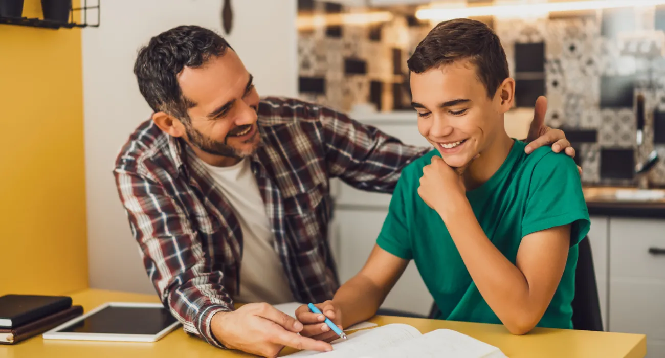 Father helping son with homework at kitchen table, sharing a happy and supportive moment together