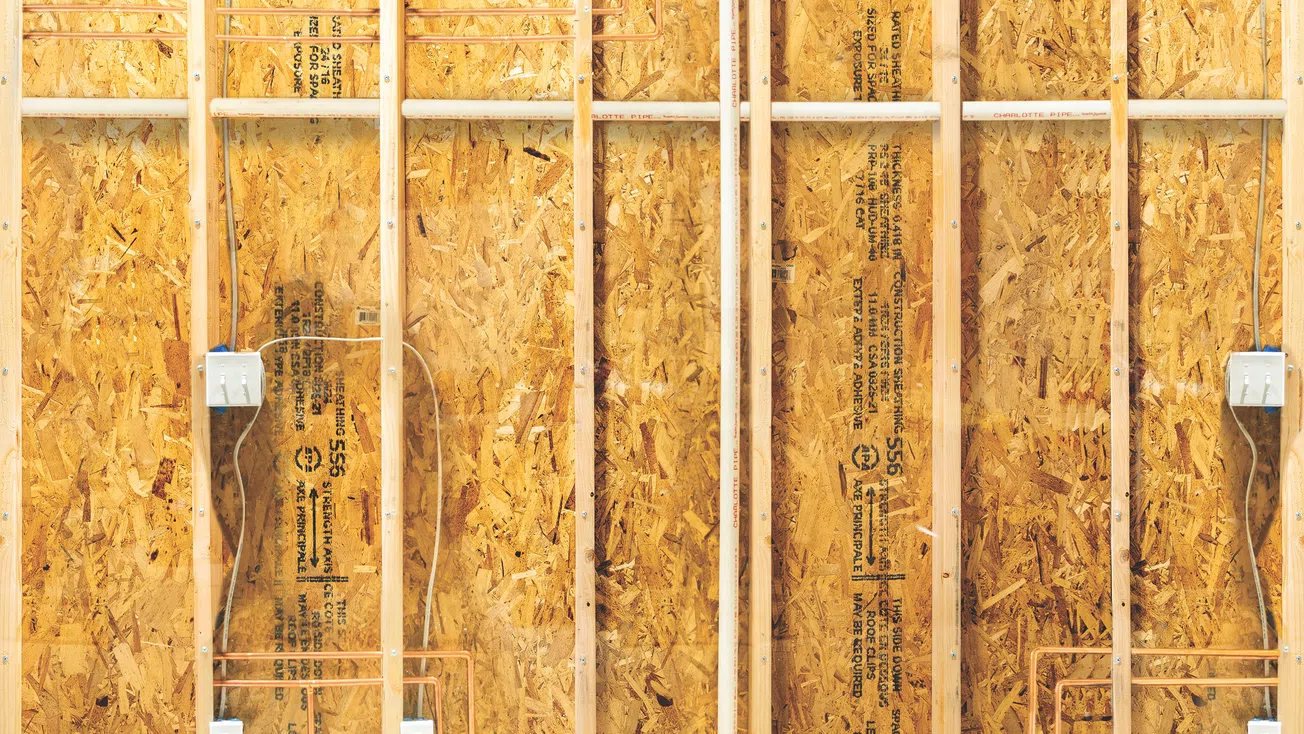Interior wall framing with plywood sheathing, electrical wiring, and outlet boxes during construction.