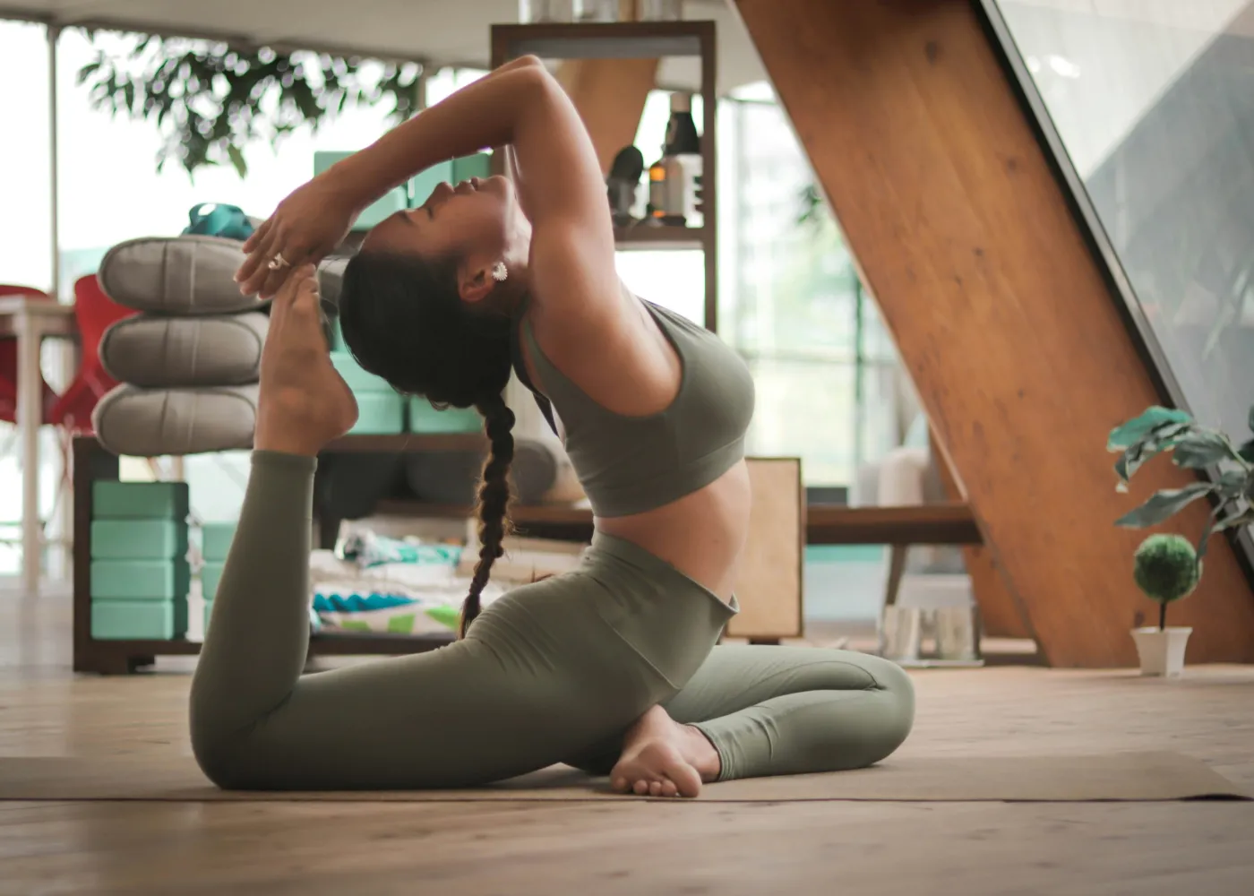 Woman in green workout clothes performing a deep backbend yoga pose indoors on a wooden floor.
