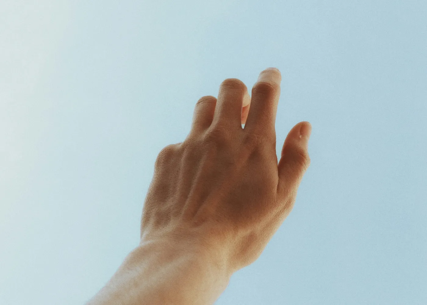 Person's hand reaching up against a clear blue sky with natural sunlight.