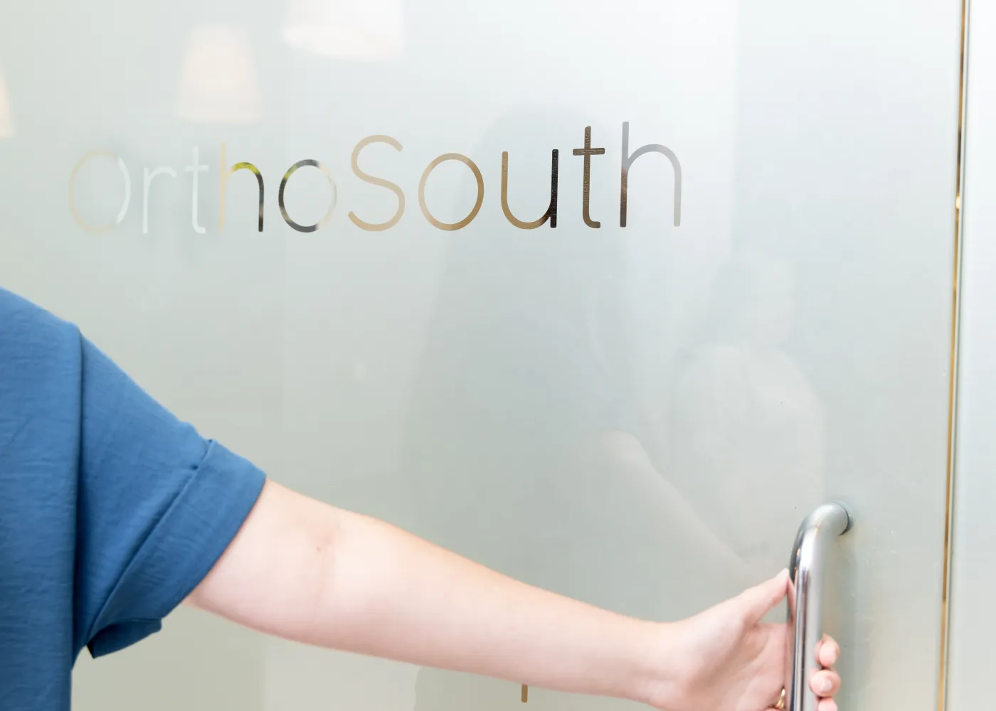 Person opening frosted glass door with OrthoSouth logo in a medical office setting.