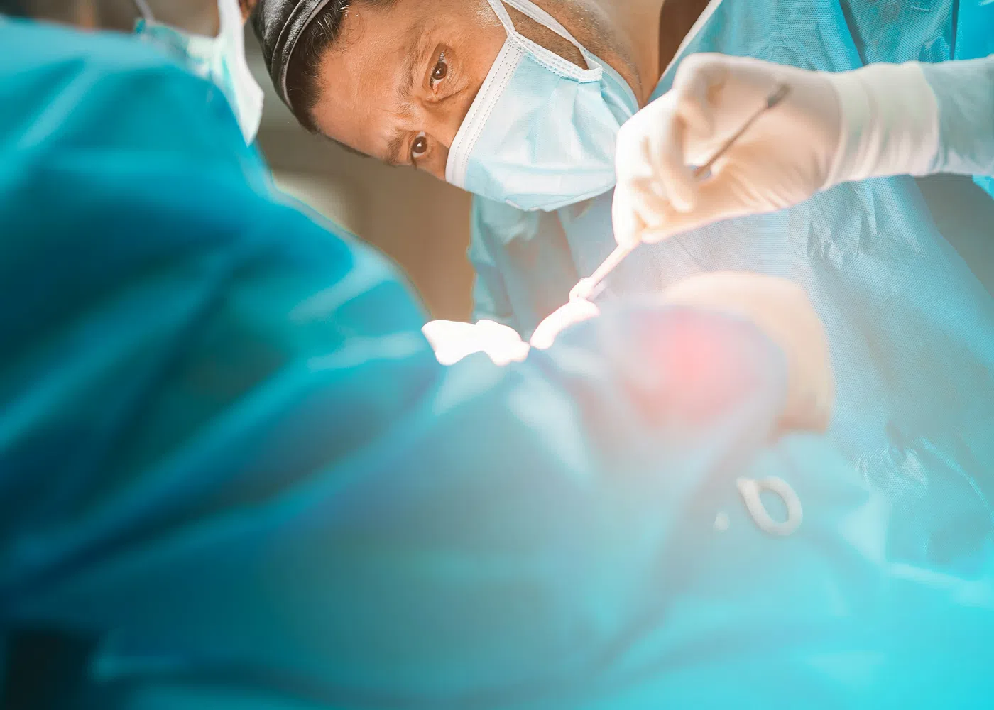 Surgeons wearing masks and scrubs performing a focused surgical operation in a bright operating room.