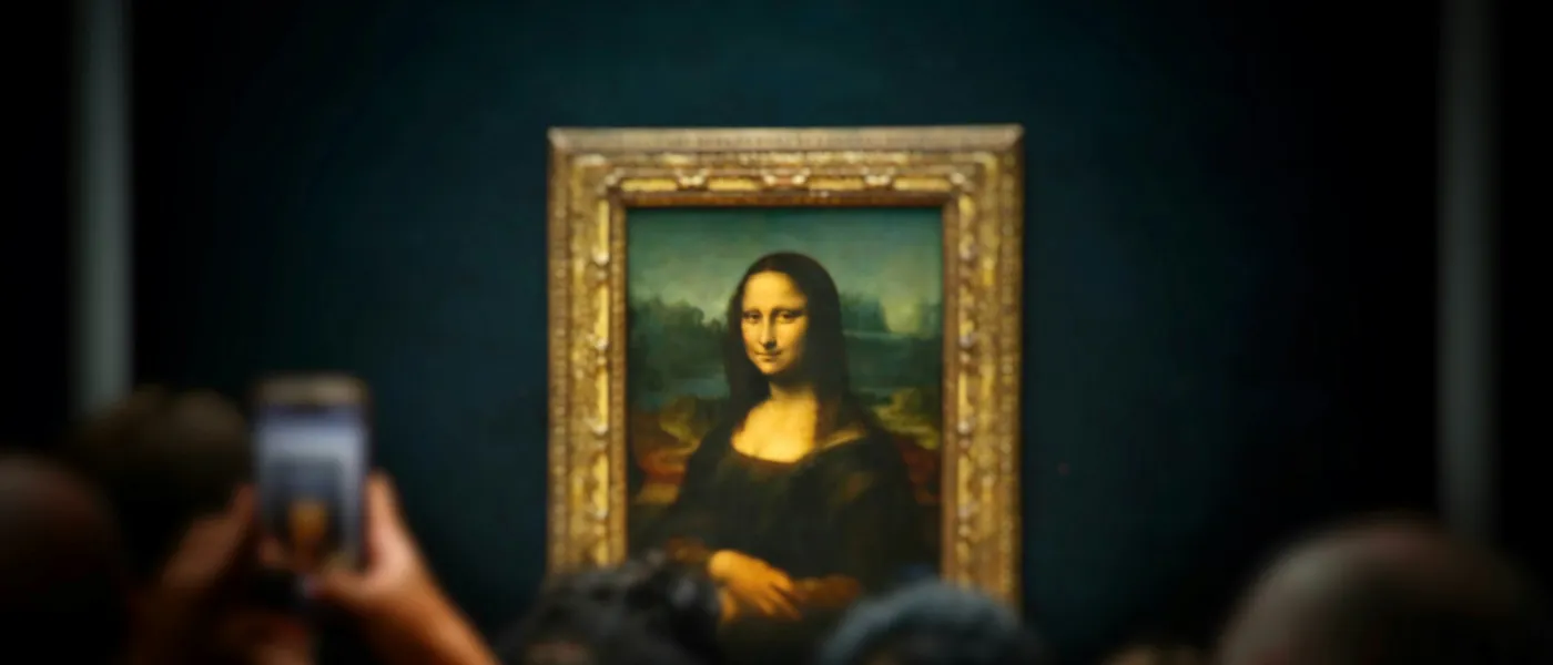 Crowd viewing and photographing the Mona Lisa painting displayed in a museum with dimmed background lighting.