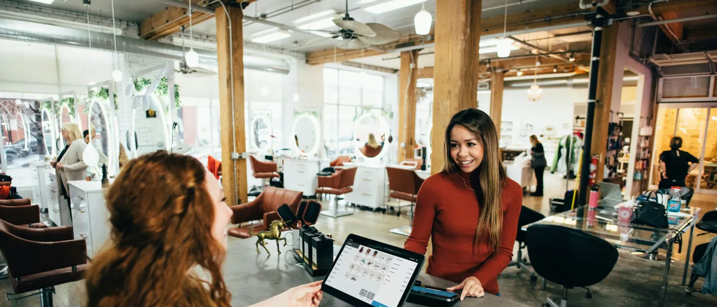 Receptionist assisting customer at modern salon with bright interior and beauty workstations in the background